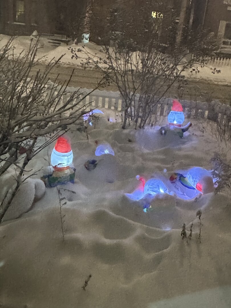 Inflatable snowmen almost completely buried by deep snow in a front yard.