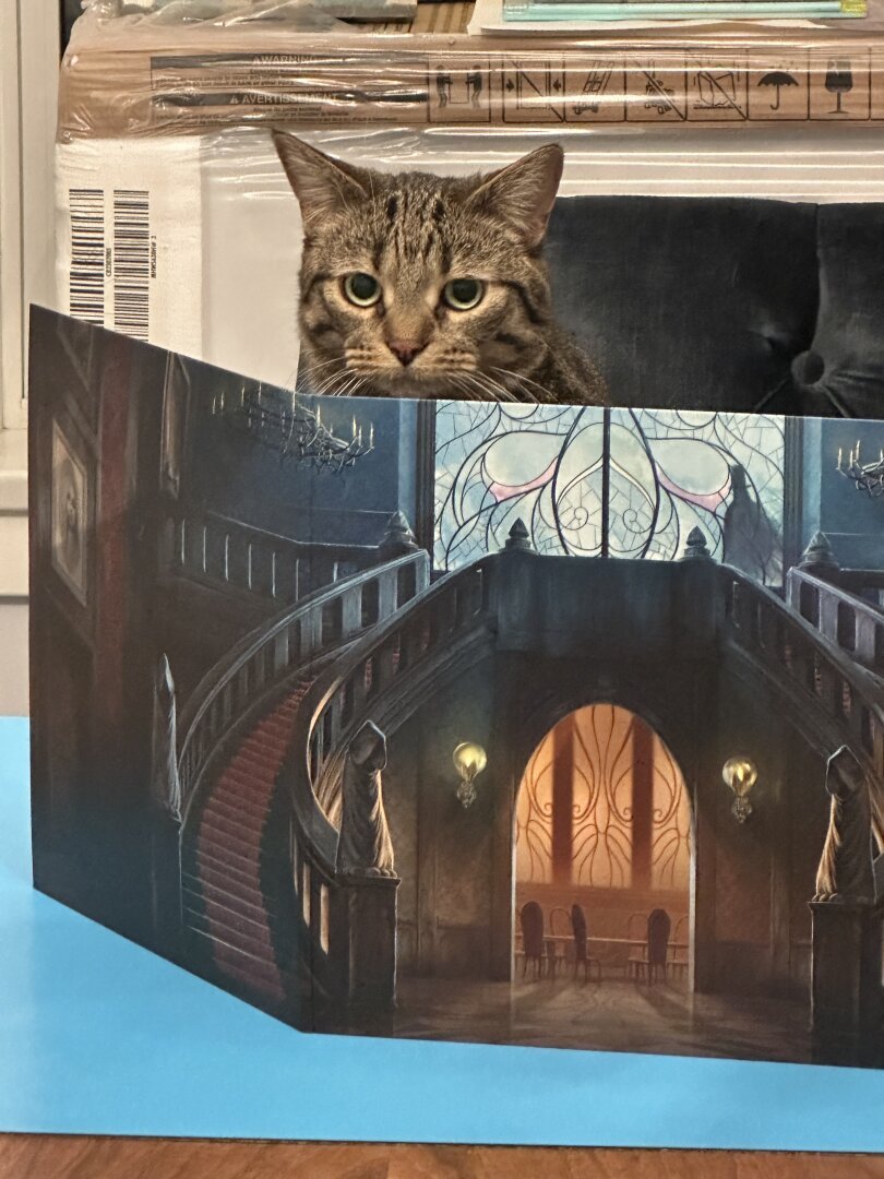 A tabby cat sitting behind a screen printed to look like a hallway and stairway in a fancy house.