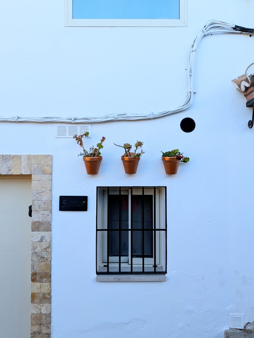 Typical white wall of Pueblos Blancos' houses with 3 small plants vases and some cables above it creating some interesting lines.
