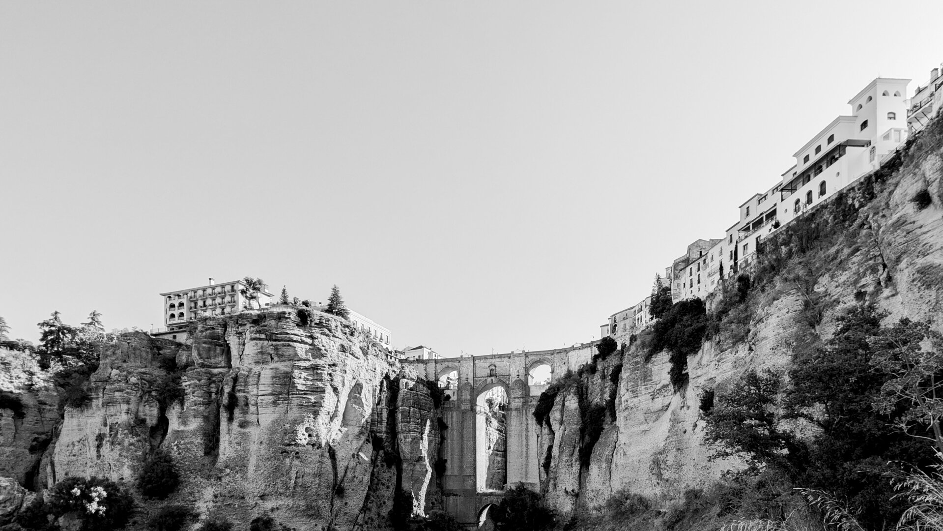 Black and white landscape of Ronda showing the Puente Nuevo in th centre, the Parador on the left and some other buildings on the right.