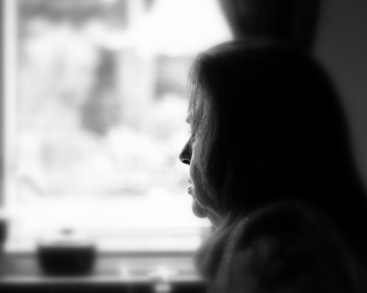 Black and white photo of woman looking out of window, silhouette in profile.