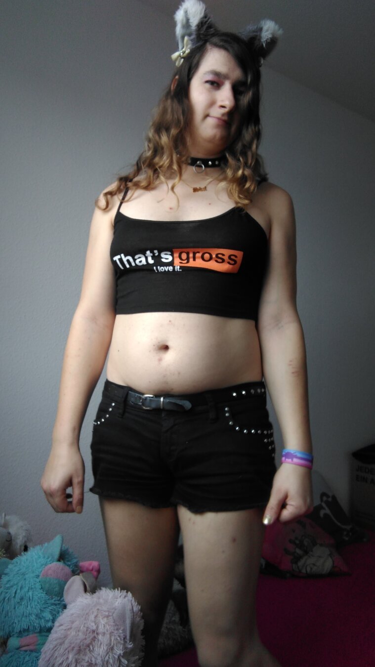 Photo of me, a white person with boobs, standing on a purple bed in front of a white wall.
I'm wearing long brown curly hair, grey cat ears with white tips, white ribbons and silver bells, a black collar with rivets and a ring for a leash, a golden necklace with a pendant of the word slut, a black crop top saying that's gross, I like it, and black jeans shorts with rivets.
On my left wrist is a catgender pride wristband and next to my right leg there are a blue and a pink alpaca plushie.