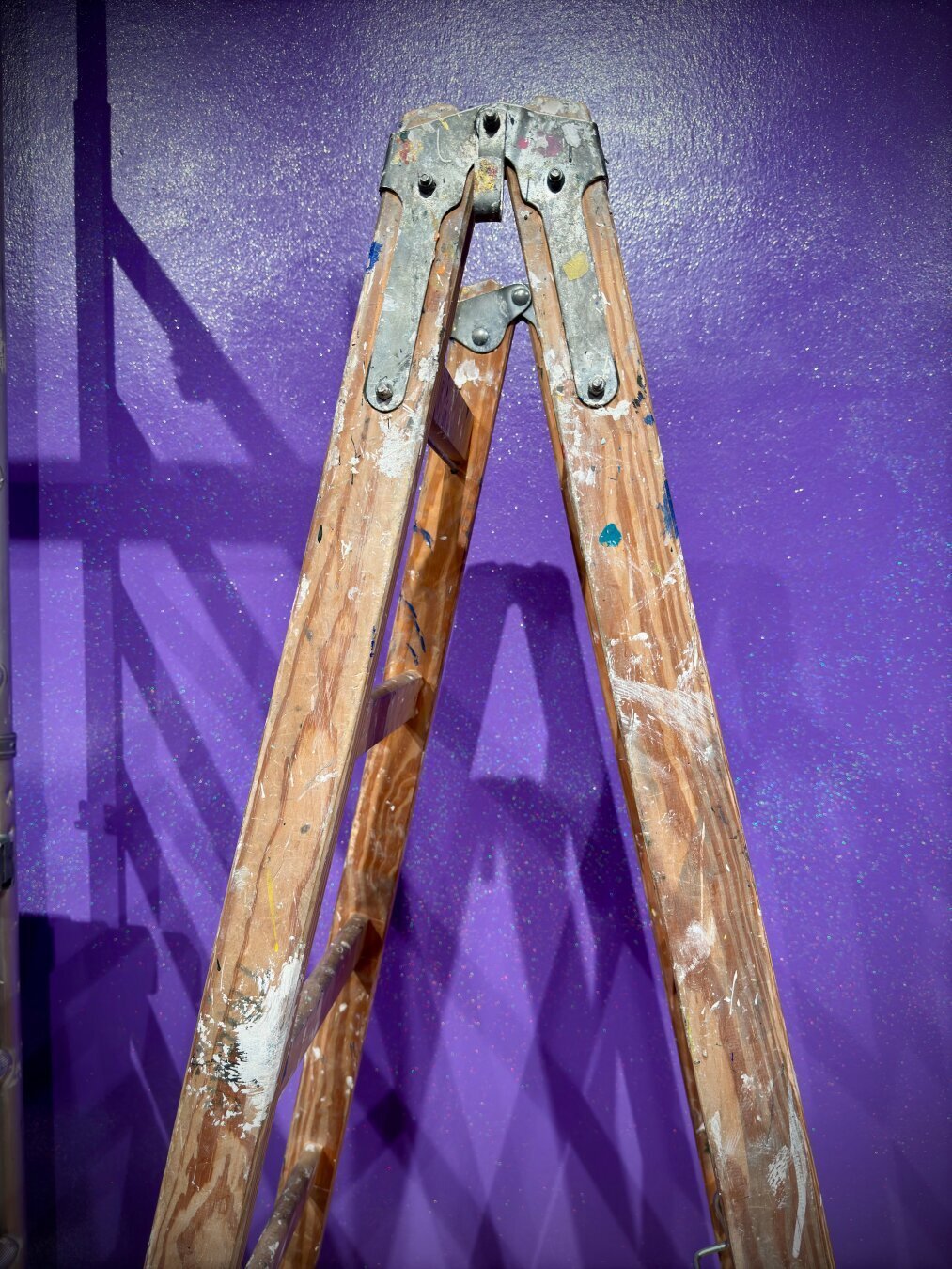 Eine Leiter aus Holt vor eine violetten Glitzerwand.