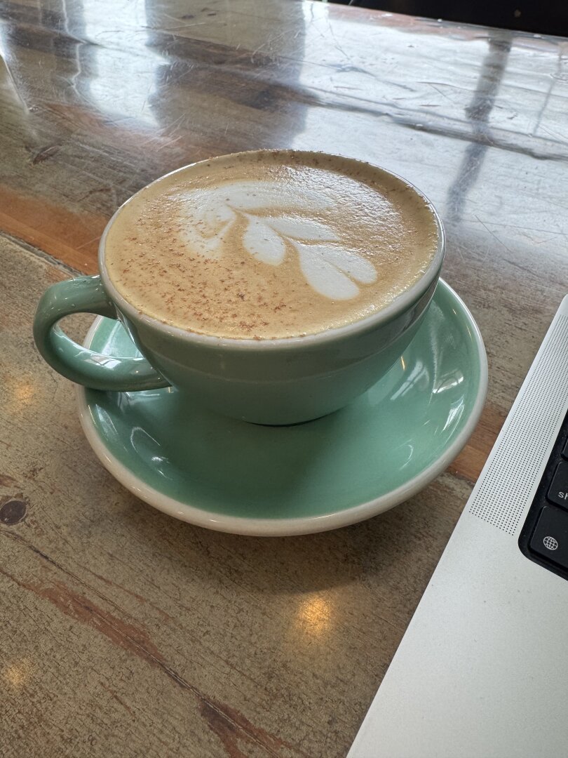 A green cup of latte with nice leaf art, next to a laptop computer.