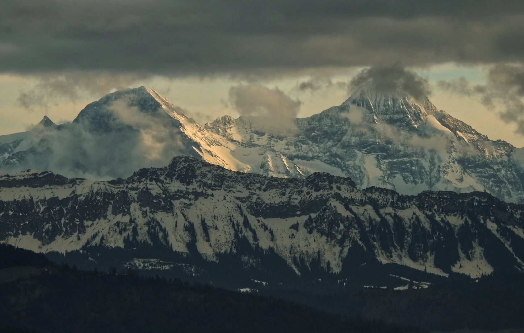 photograph: yellow-light tinged Swiss mountain tops and grey clouds