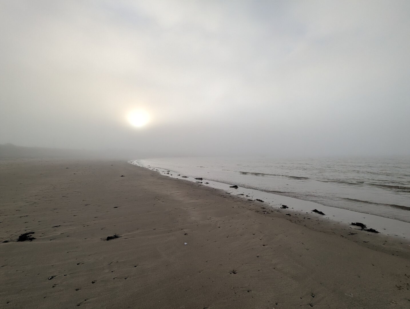 An empty Scottish beach in fog with low sun just breaking through