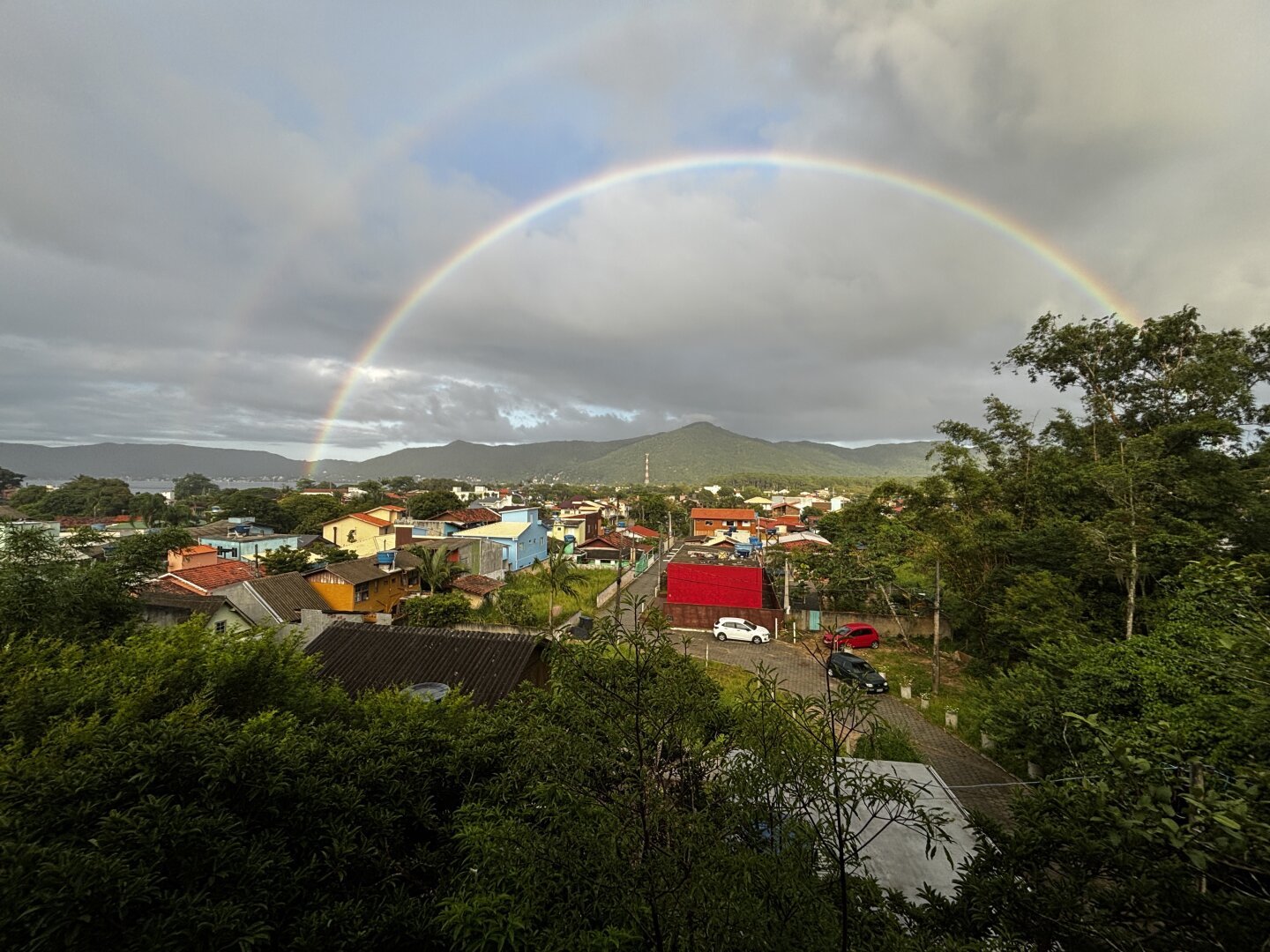 Arco-íris sobre céu com nuvens em um dia de verão sobre uma comunidade na mata atlântica brasileira.