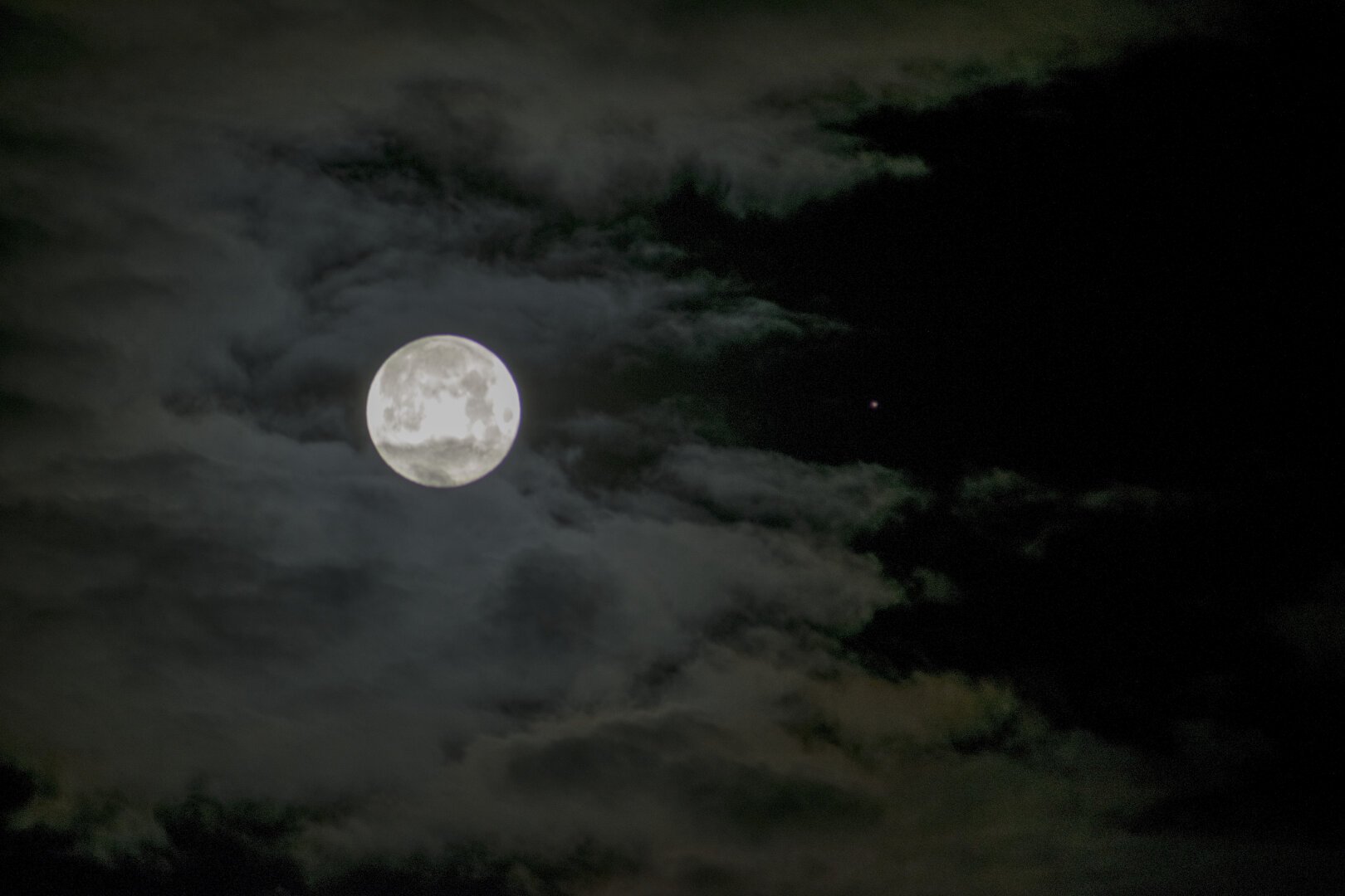 The full moon, swathed in cloud. In a clear area of sky to the right, a small reddish dot.