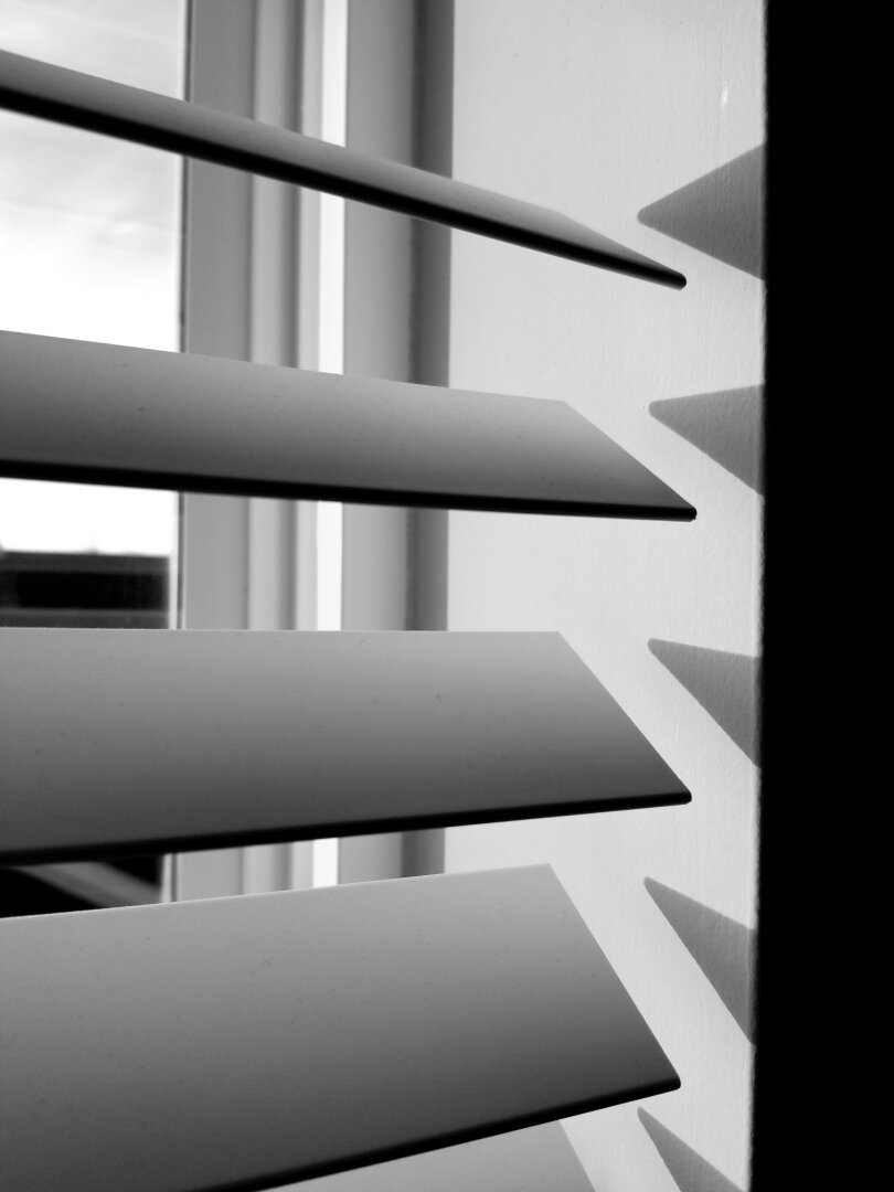 black and white photo of sunrise light coming through partially open window shades.