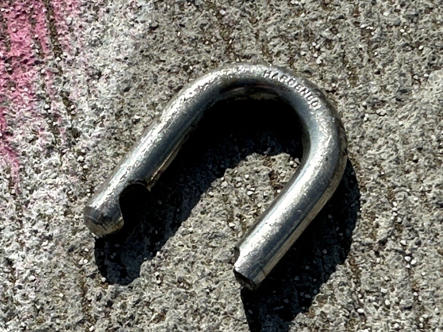 A broken shackle from a padlock lying on a cement sidewalk. The word “hardened” is written across the top.