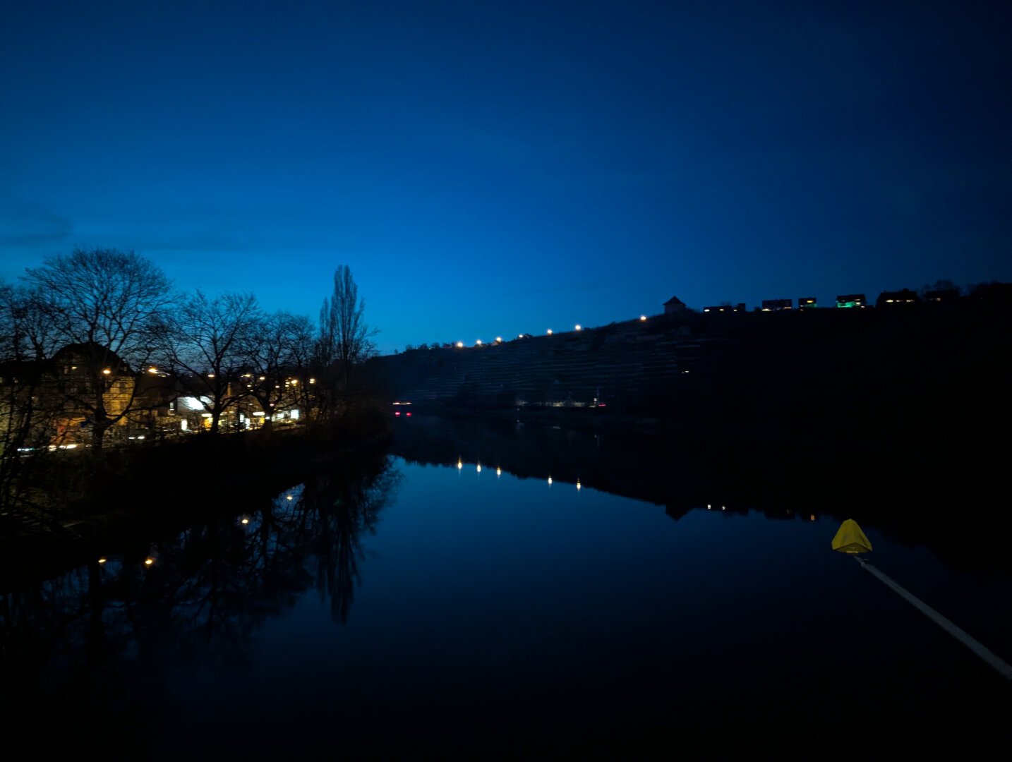Picture of the Neckar river in Stuttgart, Germany, shot from a bridge. In the background you can see vineyards and their reflection in the water.