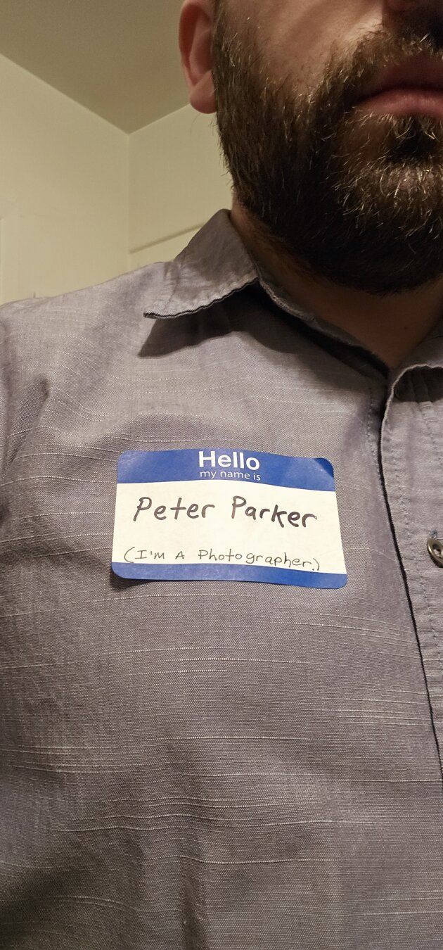close of a man in a dress shirt with a nametag that says peter parker