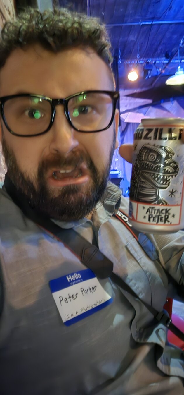 a bearded man in glasses with a nametag that says peter parker holding a beer that says attack peter