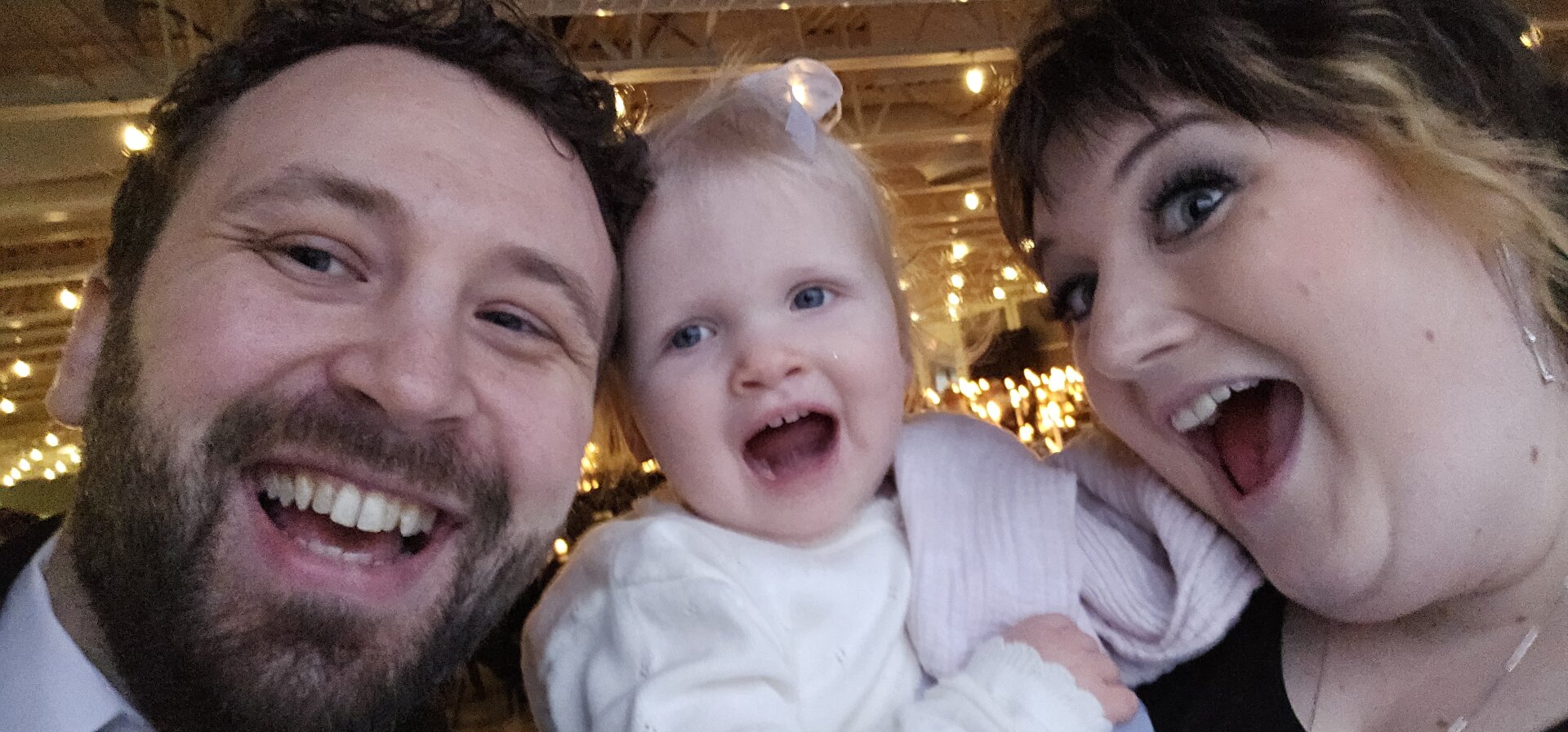 In a bright room, a formally dressed man and woman are together with a baby, smiling and sharing a tender moment filled with joy and connection.