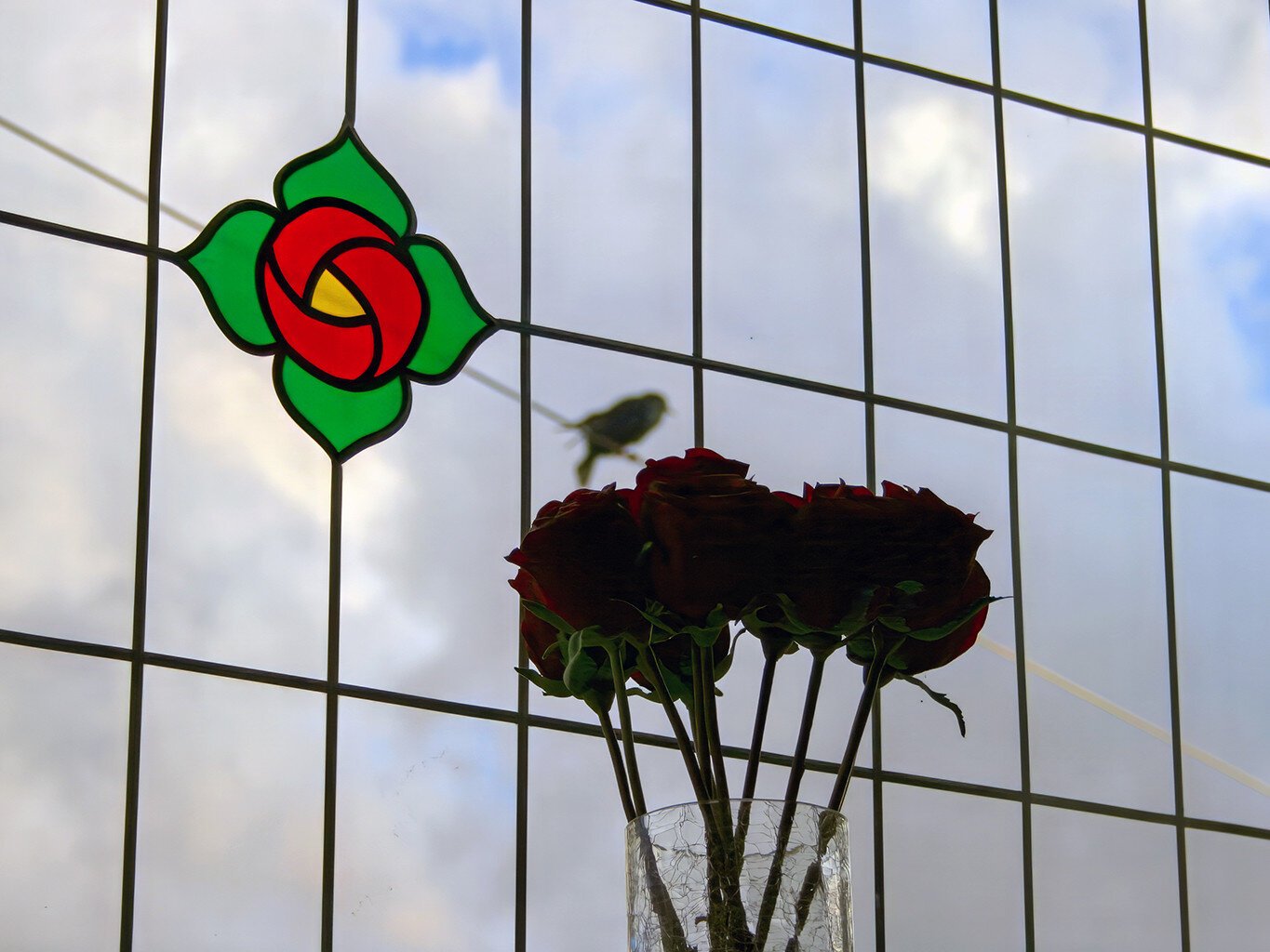 Roses in the windows.  There is also  a stained glass effect rose on the windows.  A small bird sits on the telephone wire outside and is perfectly framed by the lead on the glass.