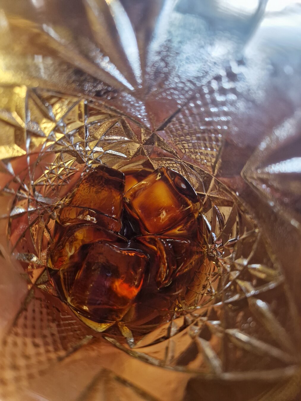 A close-up into a glass containing a few ice cubes and a small amount of cold brewed coffee.