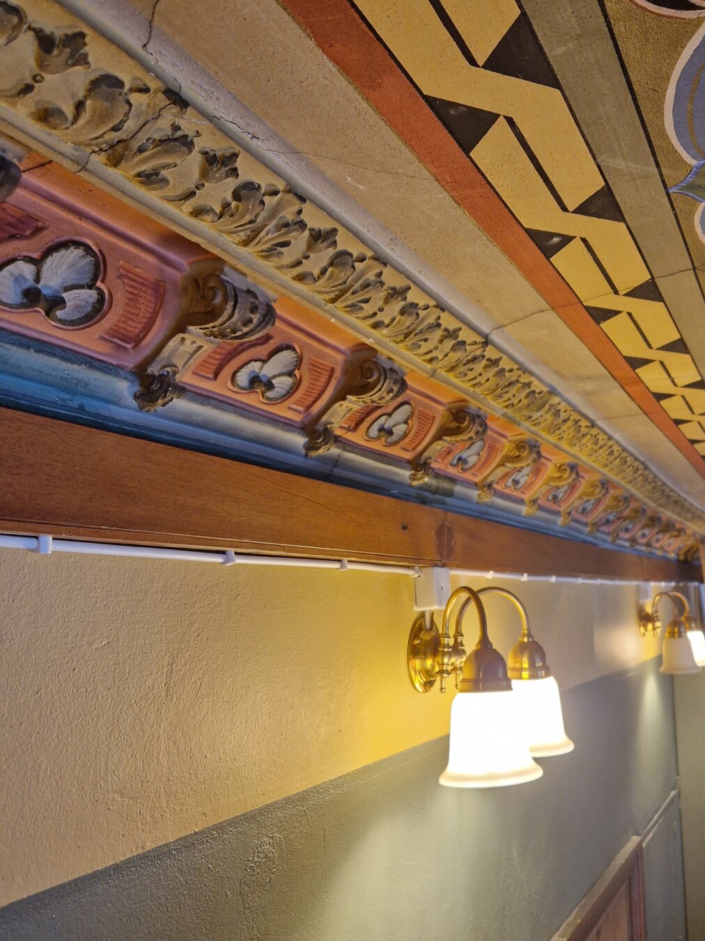 Warmly lit corner showcasing part of the painted ceiling. Mostly terracottas and blues.