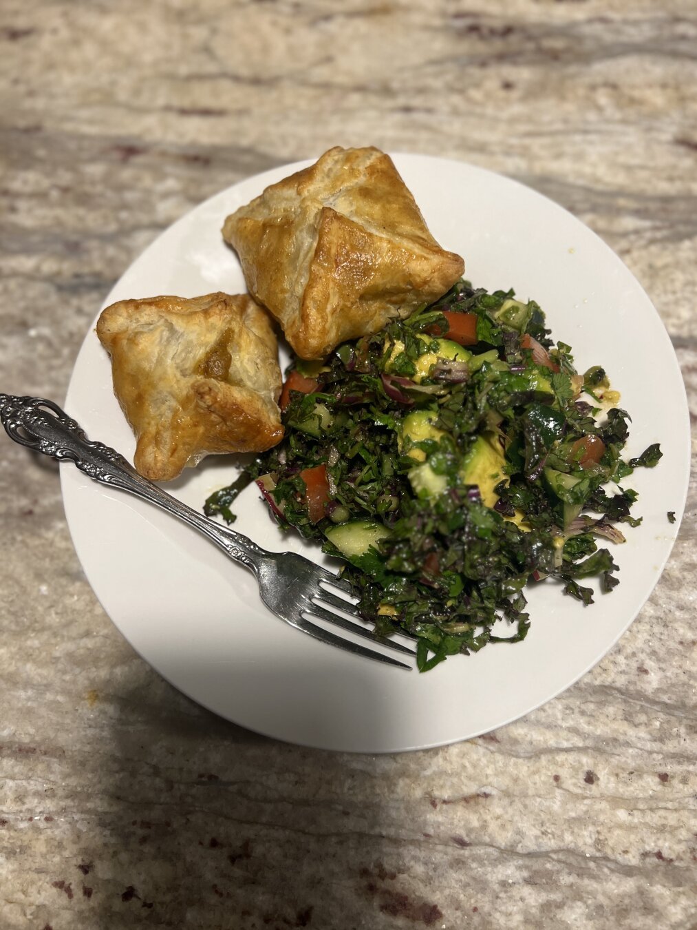 Cooked samosas on a white plate with a green salad and a fork