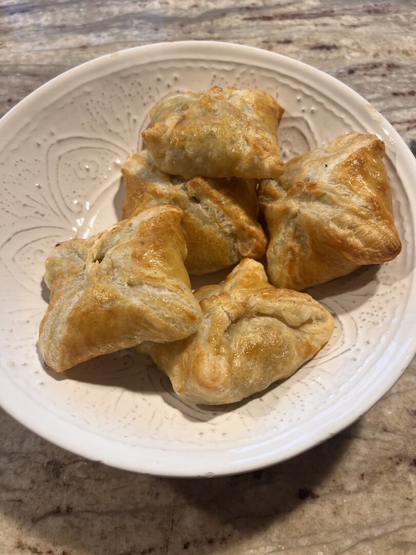 Four baked samosas in a cream bowl