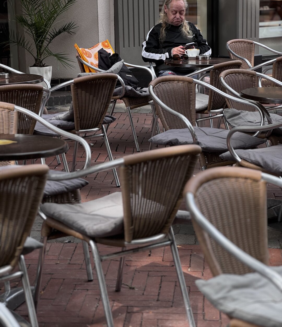 Older man sitting on a metallic chair in a café and staring in his mobile.