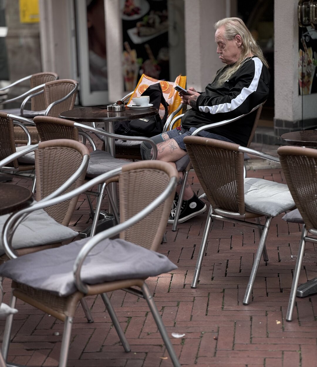 Older man sitting on a metallic chair in a café and staring in his mobile.