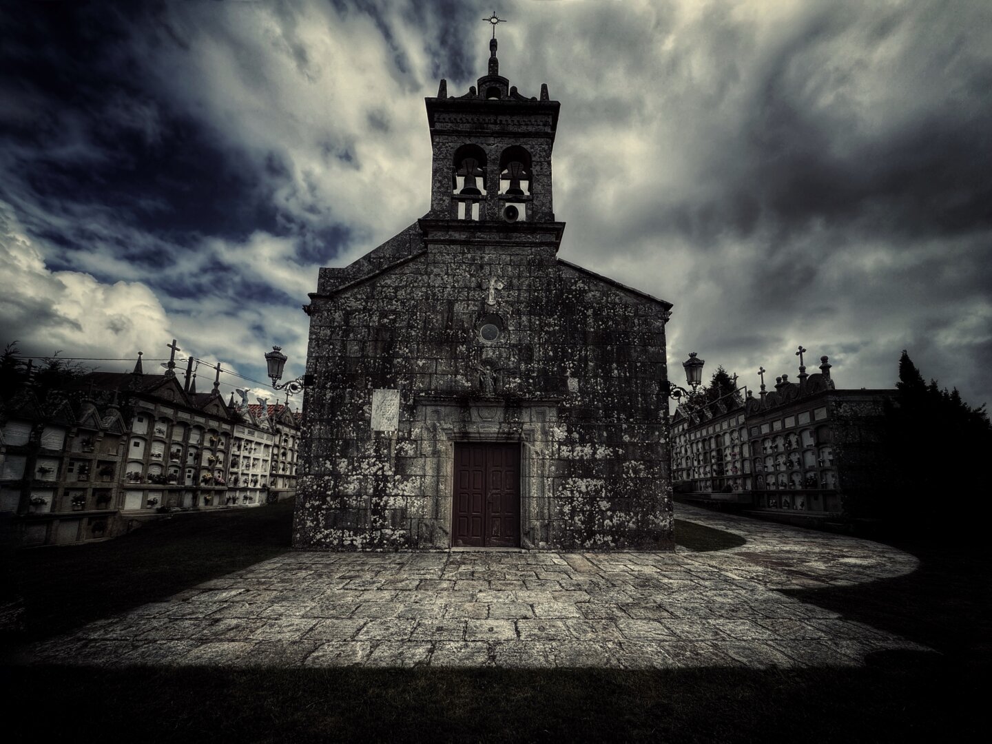 Eine Steinkirche steht prominent vor einem dramatischen, bewölkten Himmel, neben einem Friedhof mit kunstvollen Grabsteinen. Die Szene vermittelt eine düstere Atmosphäre.