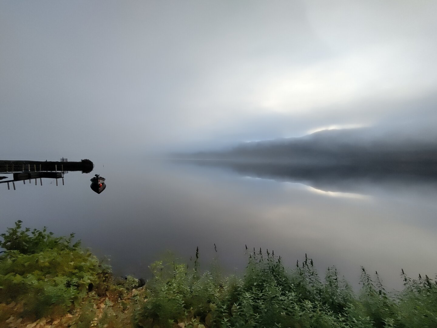 Photo of Loch Ness, early morning 12 October 2025 . Covered in fog, a small boat on the left and mountains on the right. Ford Augustus