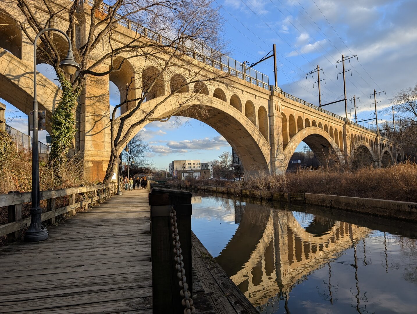 A bridge spanning a narrow canal in Philadelphia. It's a sunny day and the bridge is reflected in the calm water of the Manayunk canal.