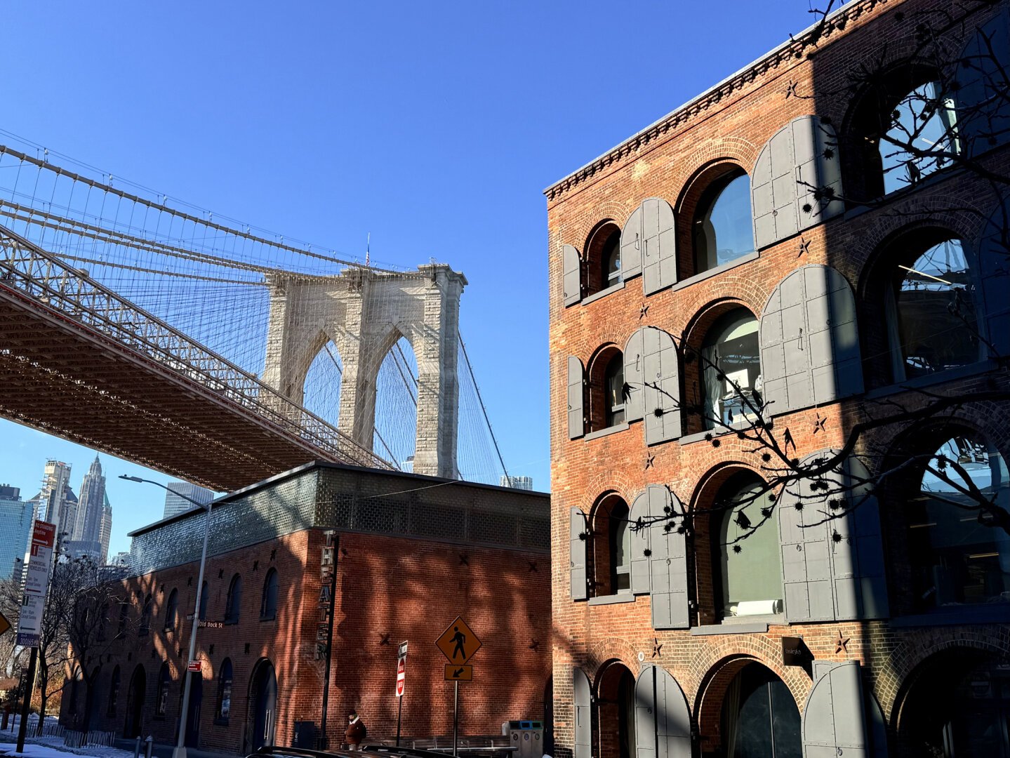 Brooklyn bridge over buildings in Brooklyn. Buildings are brick and dappled with sunlight.