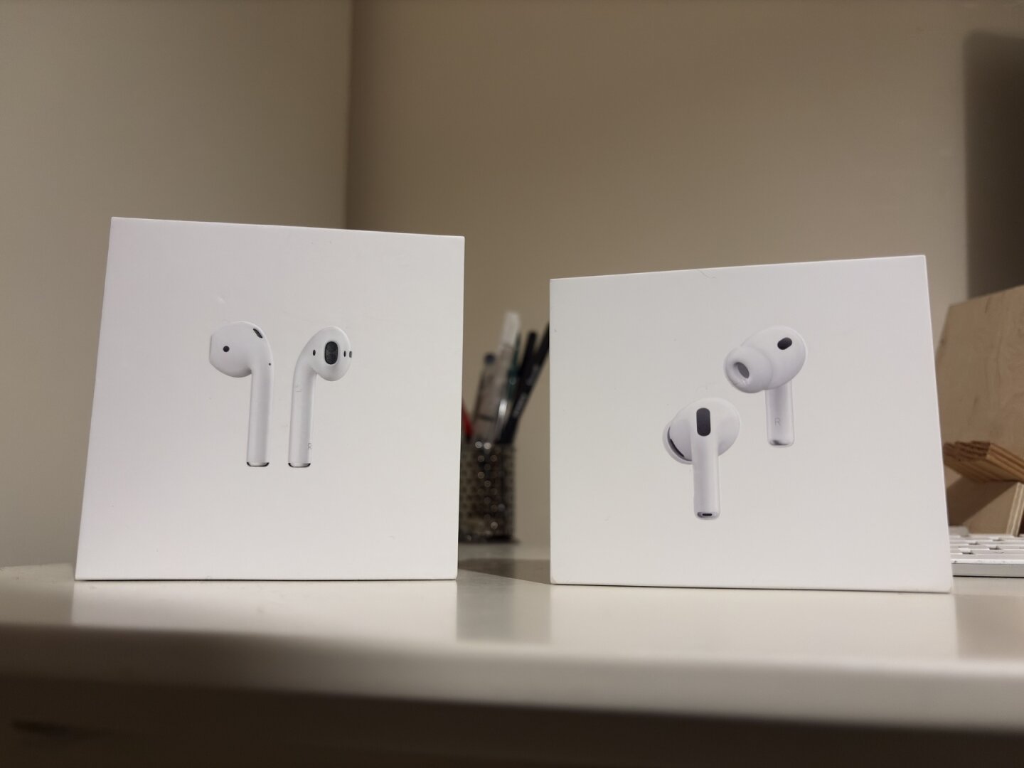 Two boxes displaying different models of AirPods are placed on a white surface. (Left are AirPods 2nd generation, right are AirPods Pro 3rd generation.)