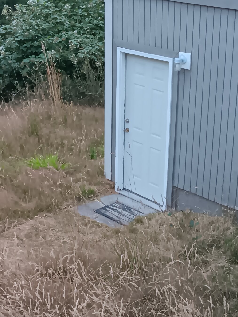 A well-fitted white door in a grey wall is firmly closed. The building appears to be in a dry field.