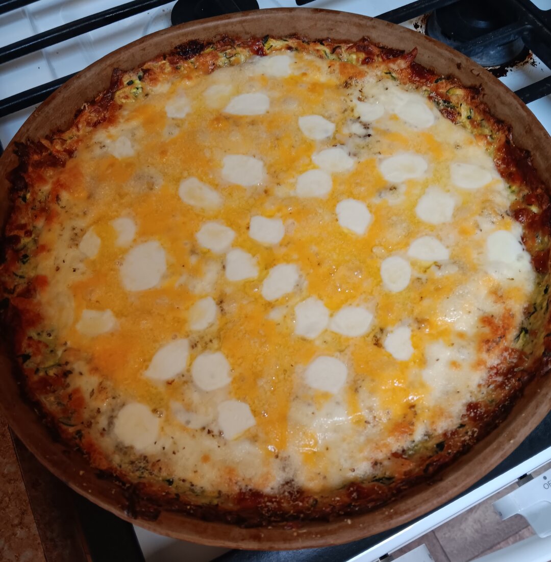 A round cheese-covered pizza sits on top of a white stove in its deep-dish pan