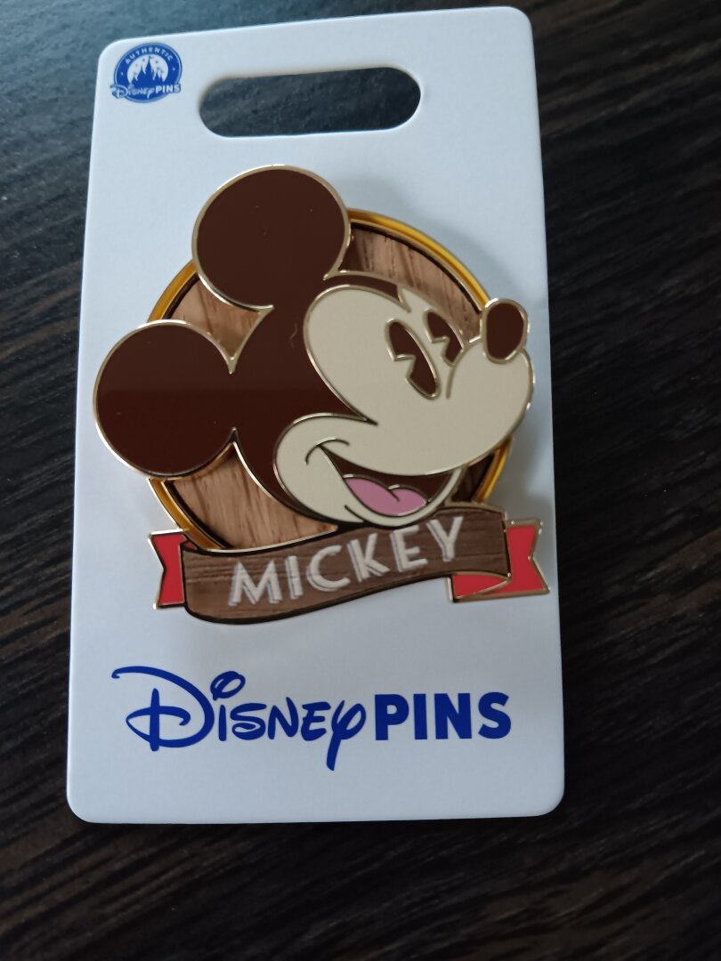 A white card holds an enamel Mickey mouse head pin on a circular wood background.