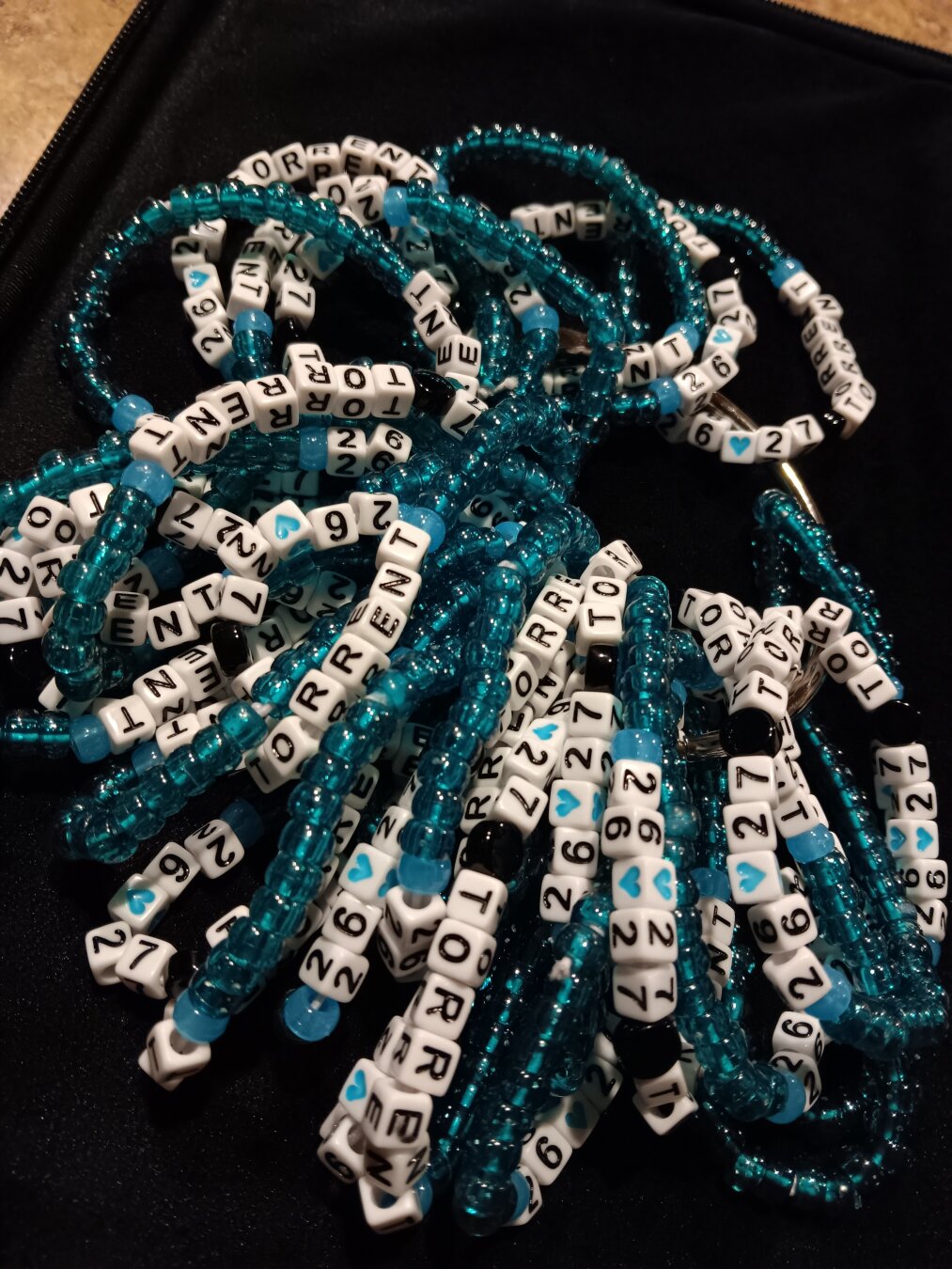 A pile of teal & white bead bracelets sits on a black surface.