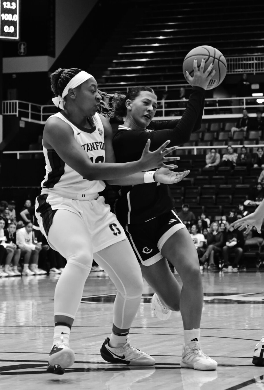 A player in white appears to hold out her hands to the player in black who has a ball a bit above the other players hands.