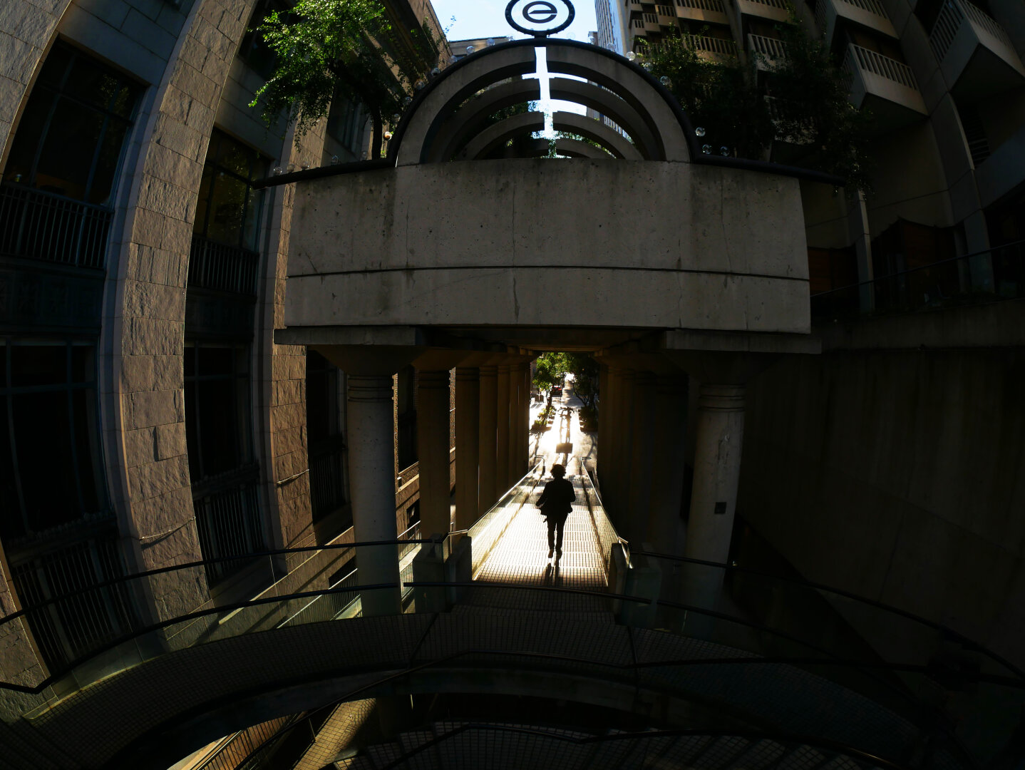 a silhouette of a figure walking along a sunlight path through tall buildings