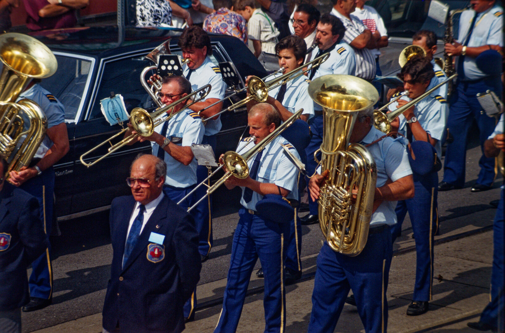 colour photo of men in uniform, playing brass instruments, moving along the street as part of a parade