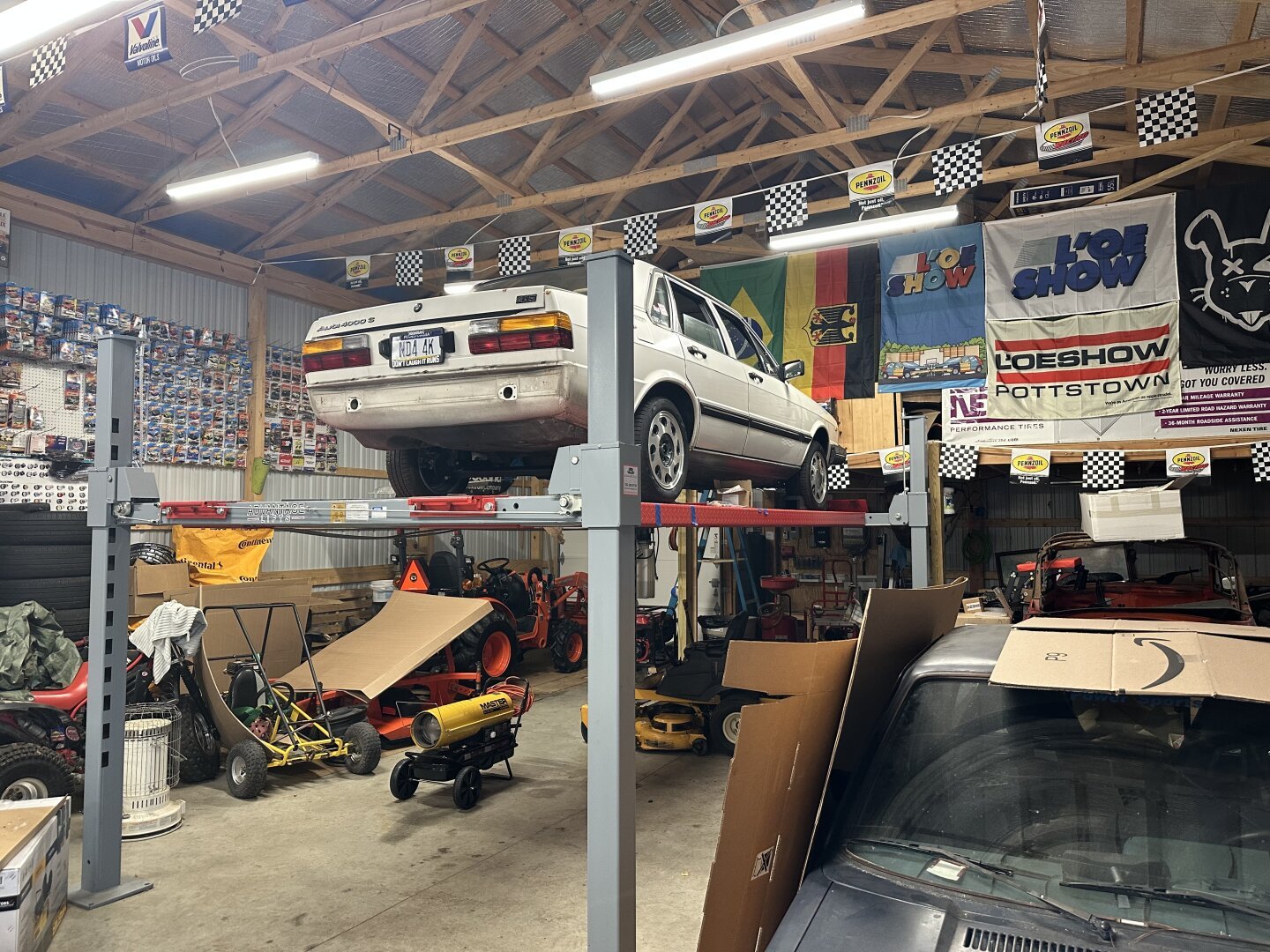 Photo of my 1982 Audi 4000 S on a four post lift in a garage. The car is white and sits on teardrop wheels from a 16v Scirocco, and the rear bumper is removed.