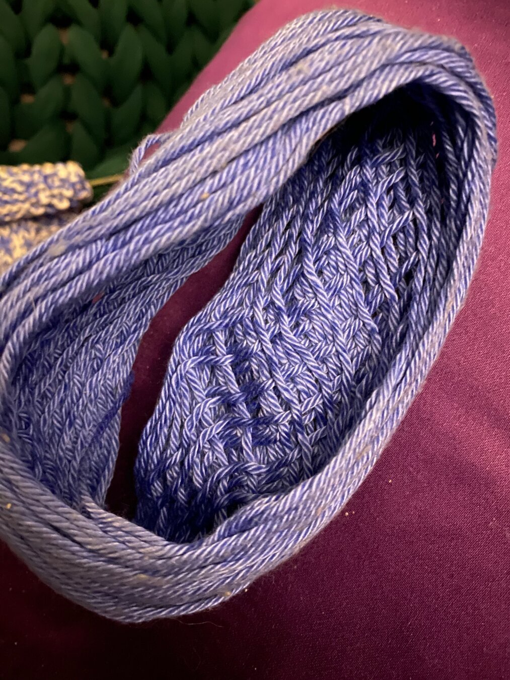 The outer-most layer of a center-pull blue yarn ball lies at an angle on a purple pillowcase, so that the inside is visible. The outer bit of the ball is just yarn wrapped straight around, but the inner bit shows evenly-spaced wraps going at 45 degree angles in both directions, making a neat crosshatch pattern.