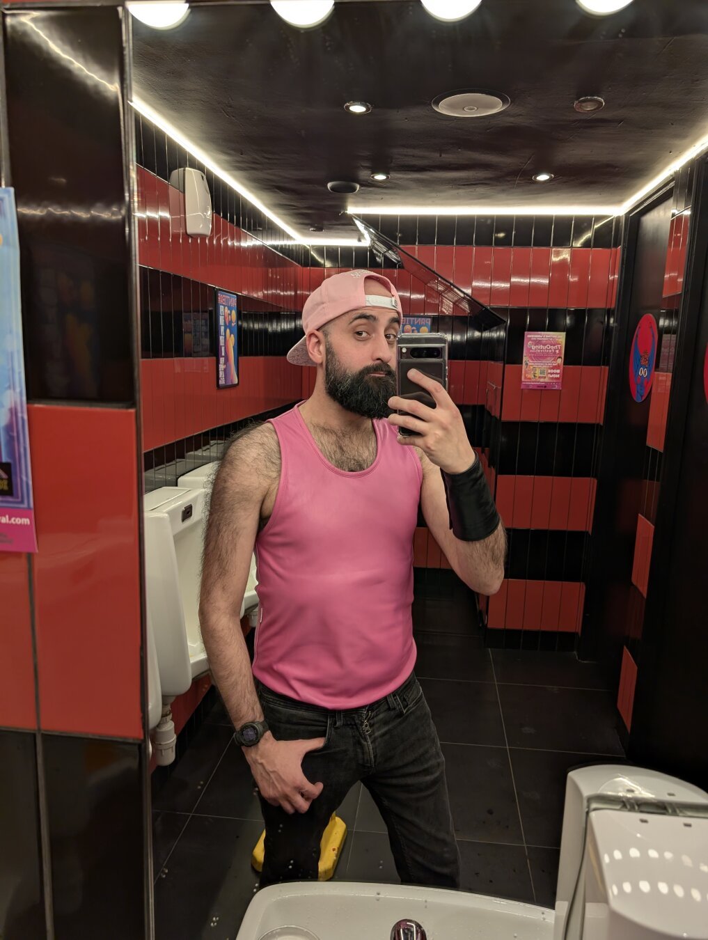 A selfie of a bearded man in a bathroom mirror. He's wearing a backward pink cap that says 