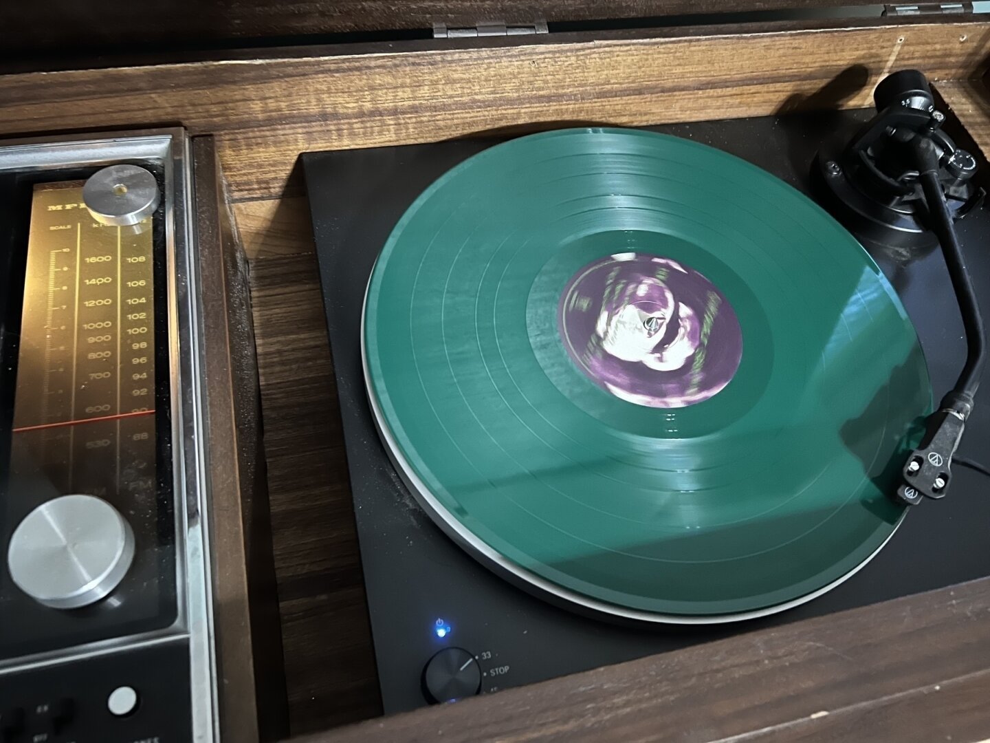 A green vinyl record is spinning on a turntable with a stereo system nearby.