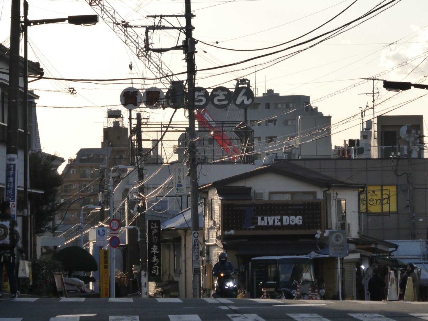 An intersection in Japan. The top of a hill and streets heading right and left down the hill, with a gentle glow from a setting sun