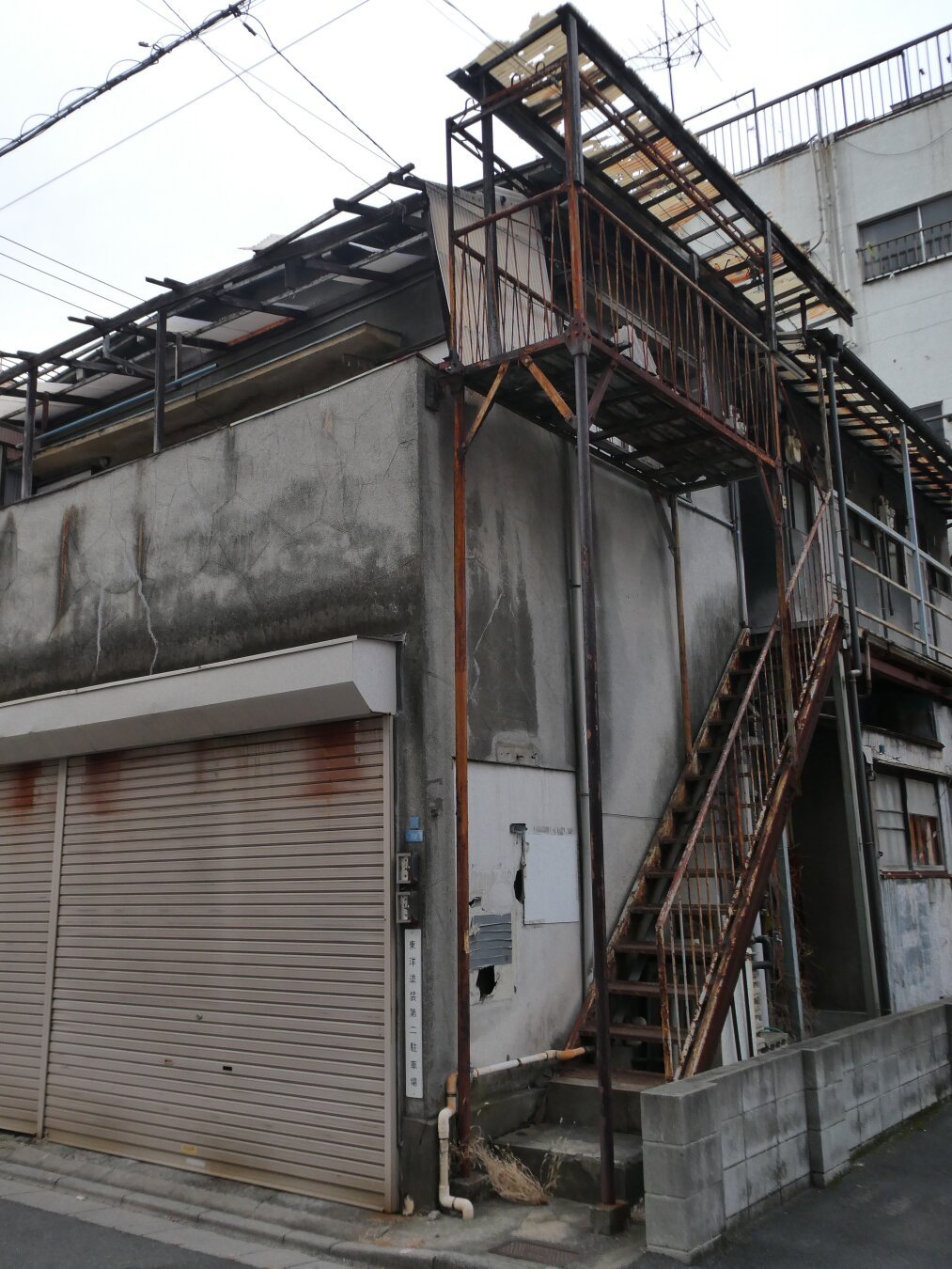 Worn stairs trail up the side of an abandoned apartment, in Tokyo. All is grey and worn