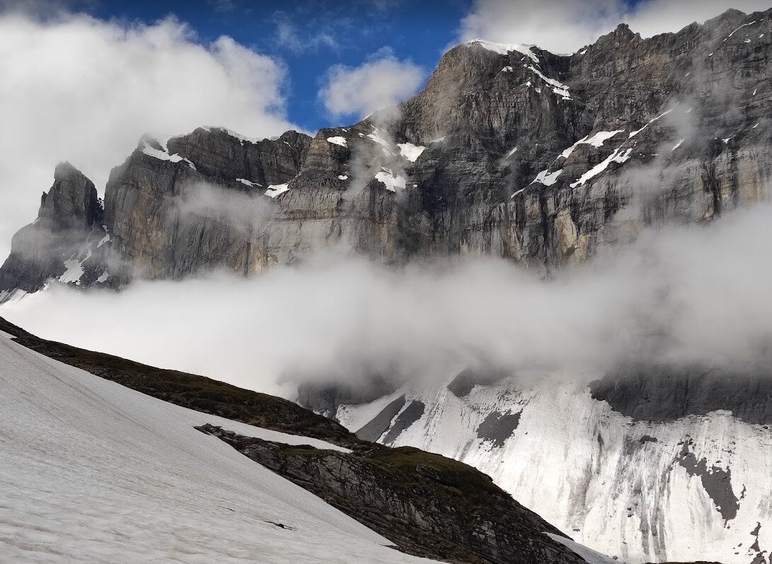 moutains with snow, blue sky, a bar of clouds in front of a cliff