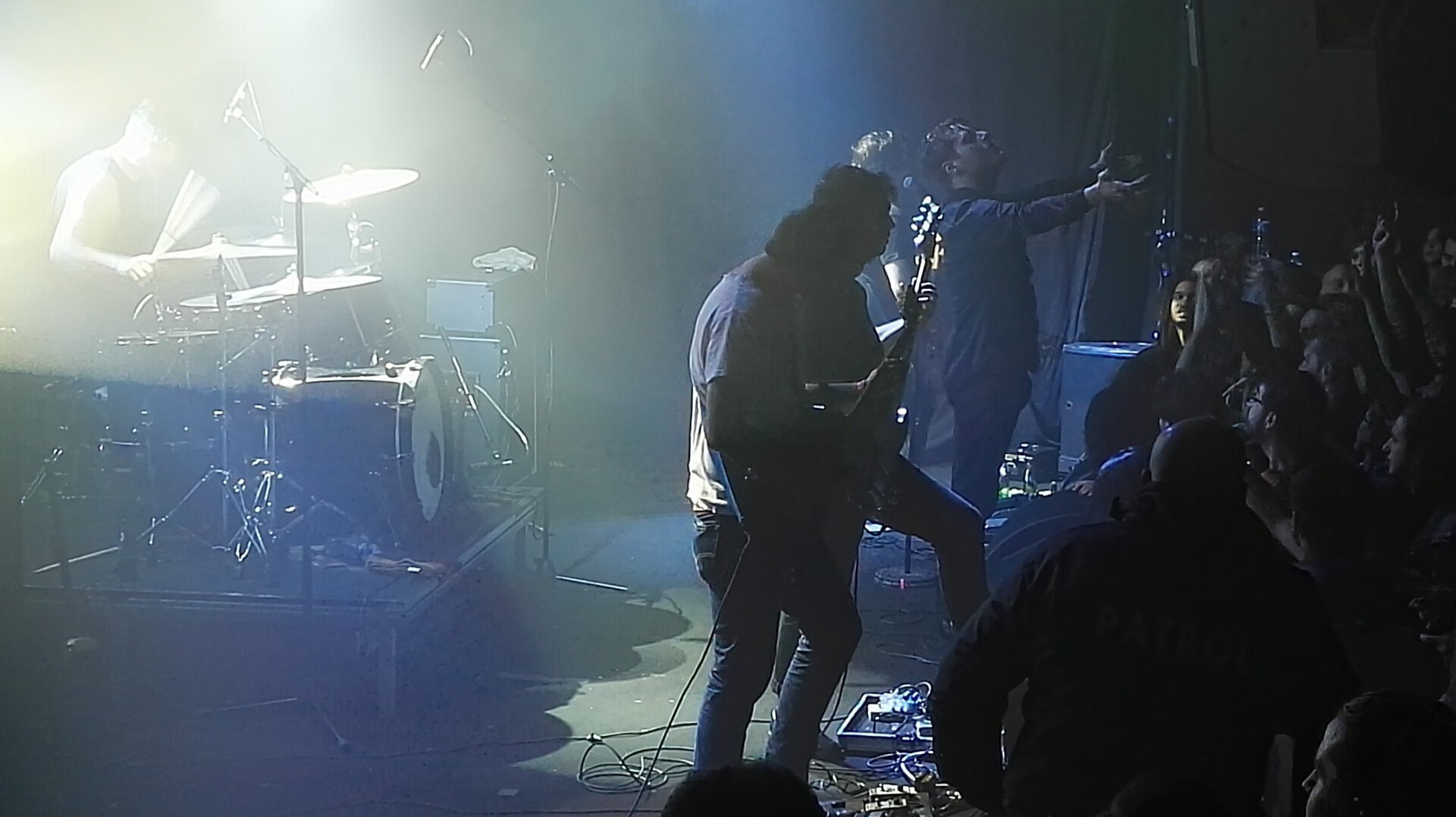 show of the post metal band, singer opening arms to the public, 2 guitarists in the dark and the drummer in the light