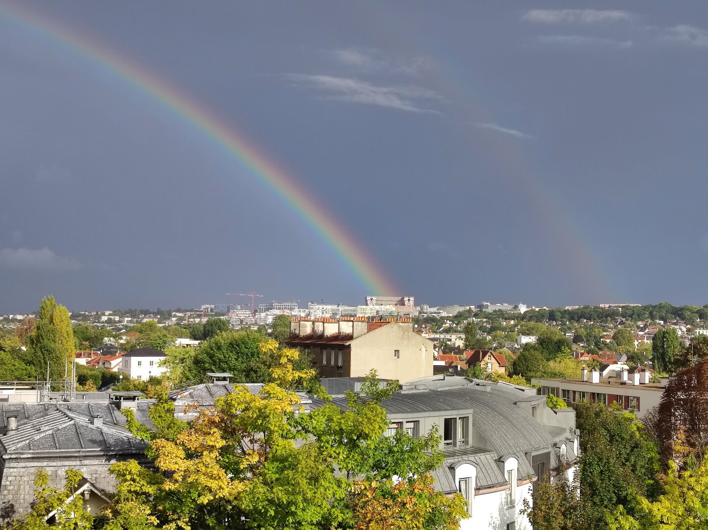 gray sky with a big rainbow over houses.