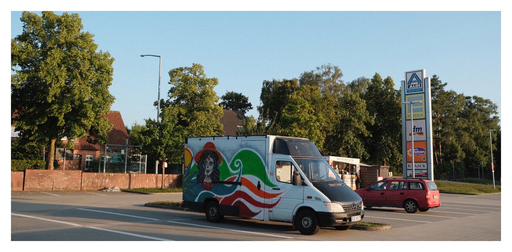 A bus with graffiti on it on a parking lot at sunset. The graffiti shows a (mexican?) girl