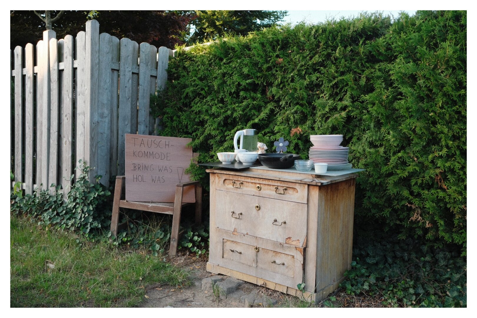 A commode with plates, a water boiler and a pan. Besides a sign saying: Exchange commode. Bring something. Get something.