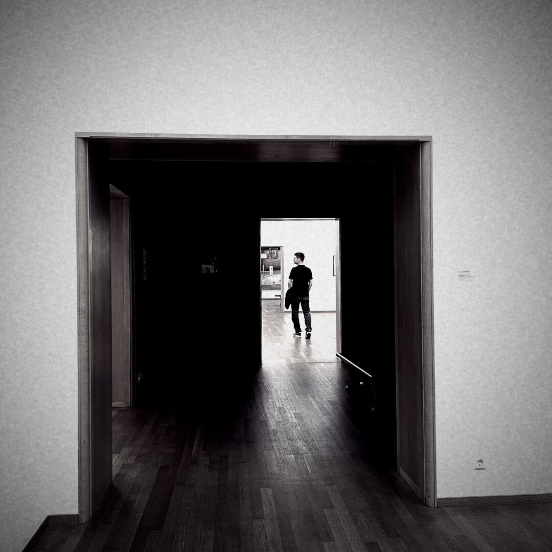 A black and white photo of a person in the background, seen through two open doors.