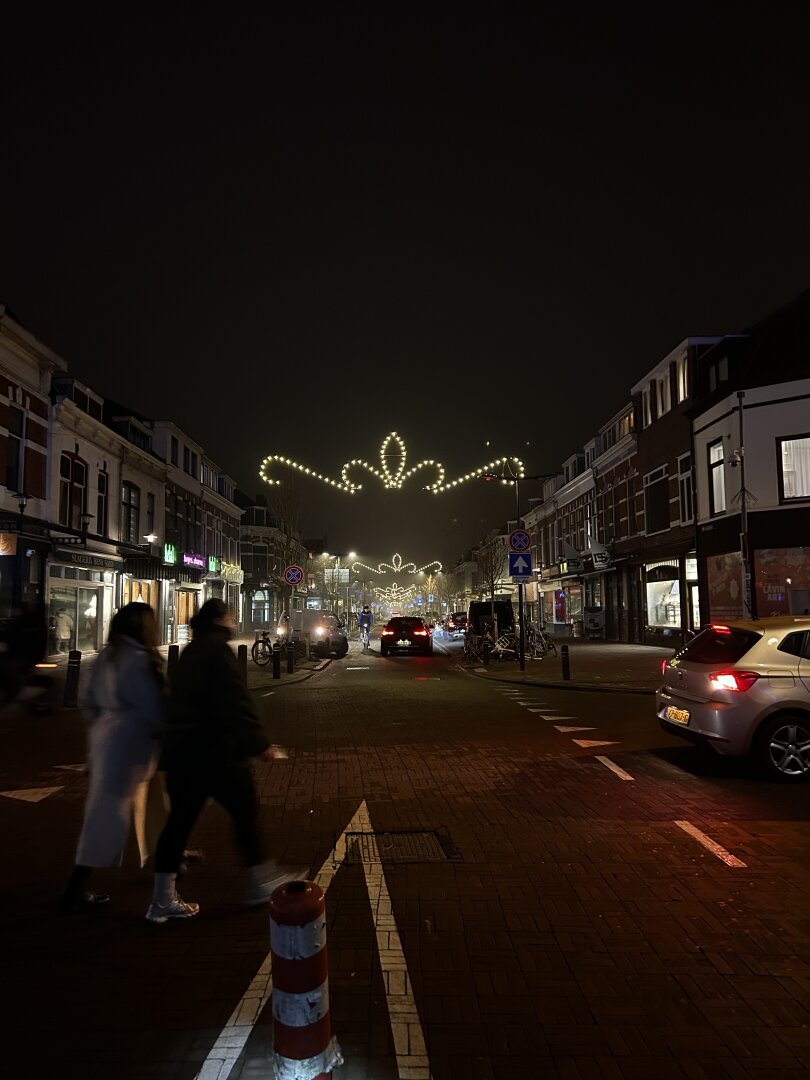 Kanaalstraat in Utrecht in de late avond. 2 mensen lopen voorbij en er hangt een feestelijke straatverlichting